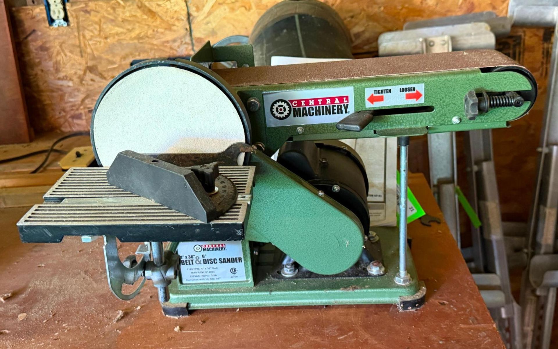 Green and black belt-and-disc sander on a wooden shelf in a workshop