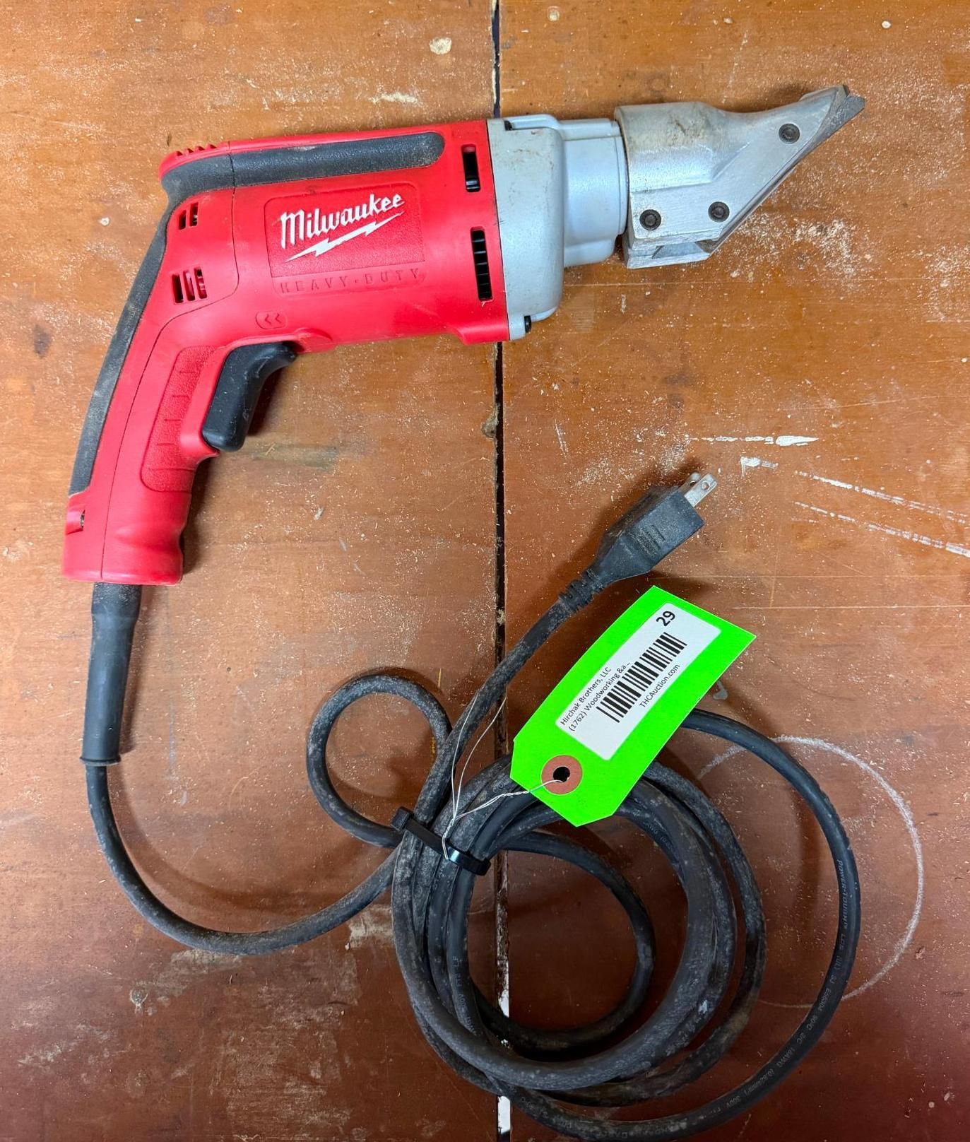 Red Milwaukee corded power tool with silver attachment and coiled black cord on a wooden surface