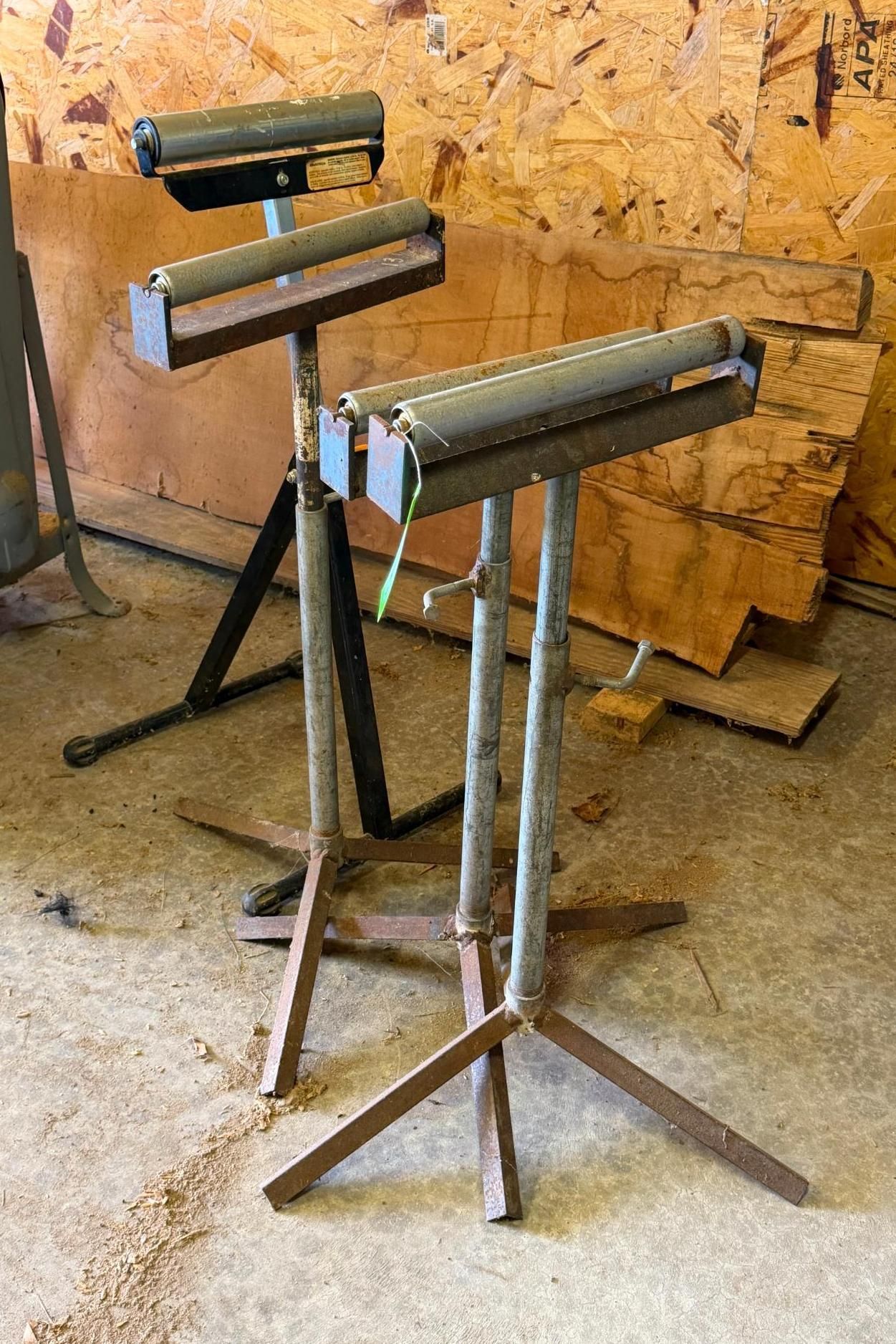 Three metal stands with rollers in a workshop, in front of a plywood wall.