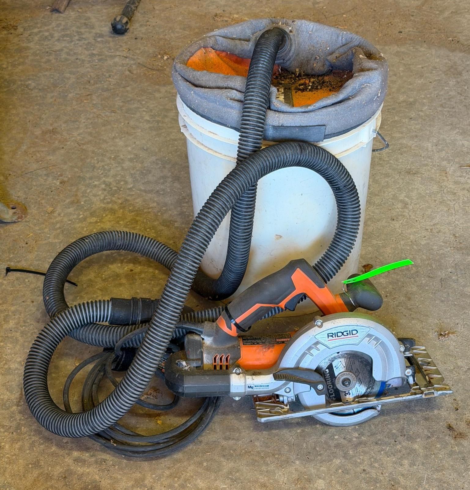 White bucket and orange cordless circular saw with black hose on a concrete floor