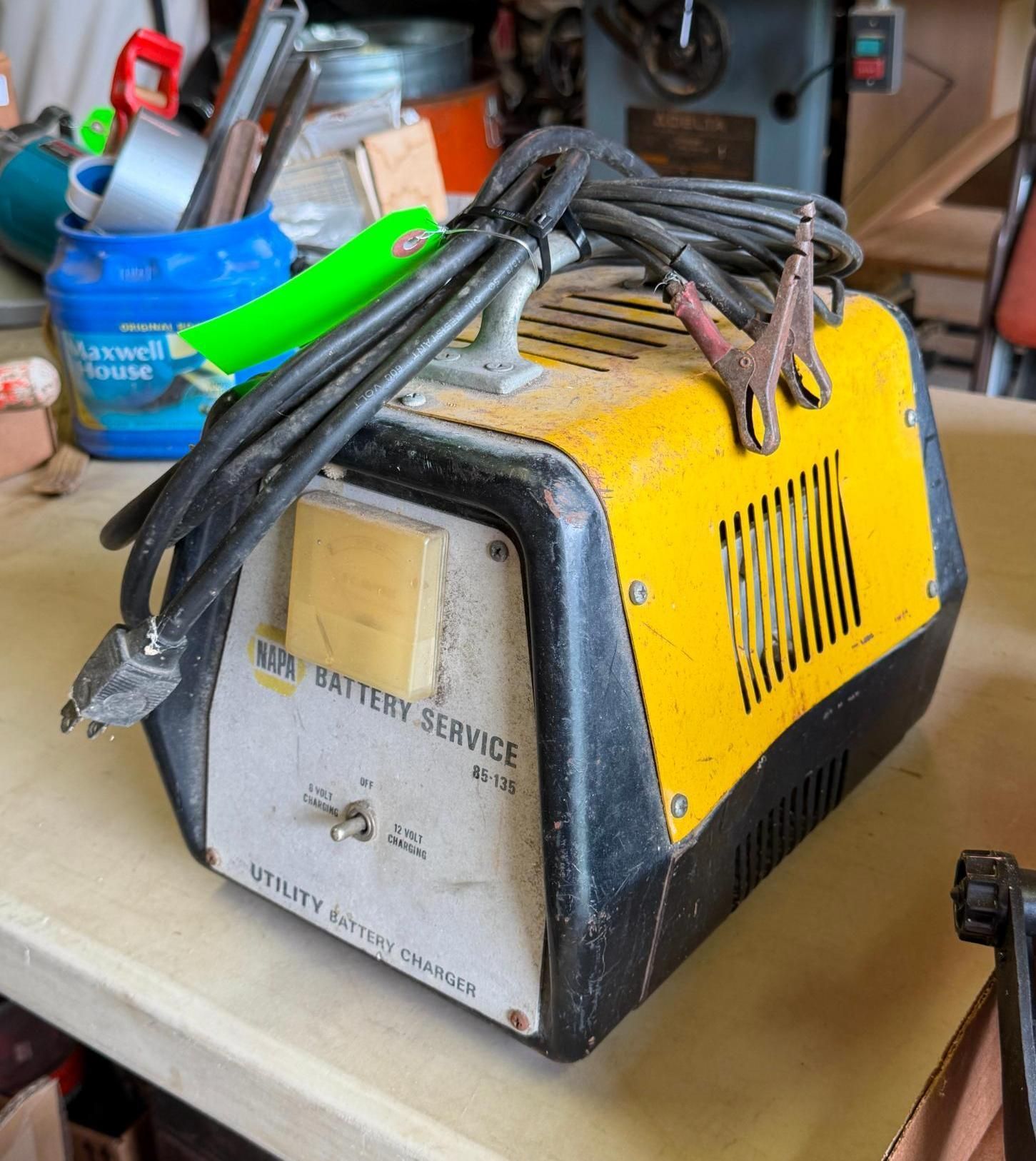 Yellow and black battery charger with cables coiled on top, sitting on a workbench.