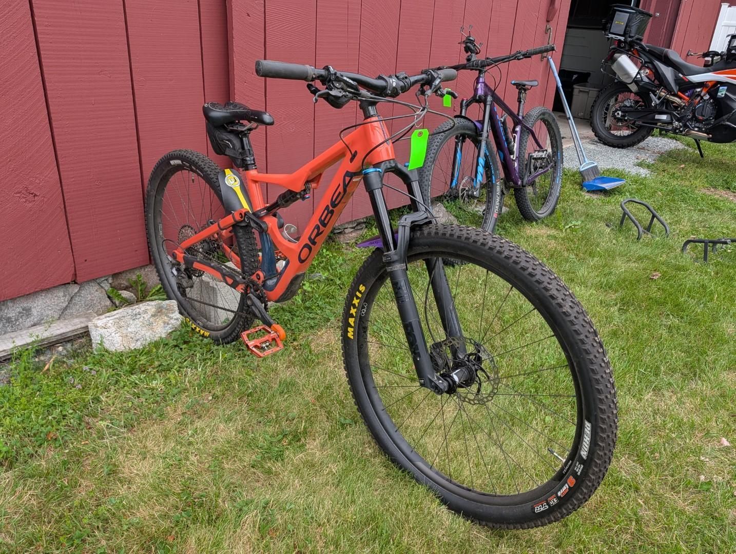 Orange mountain bike parked on grass beside a red wall