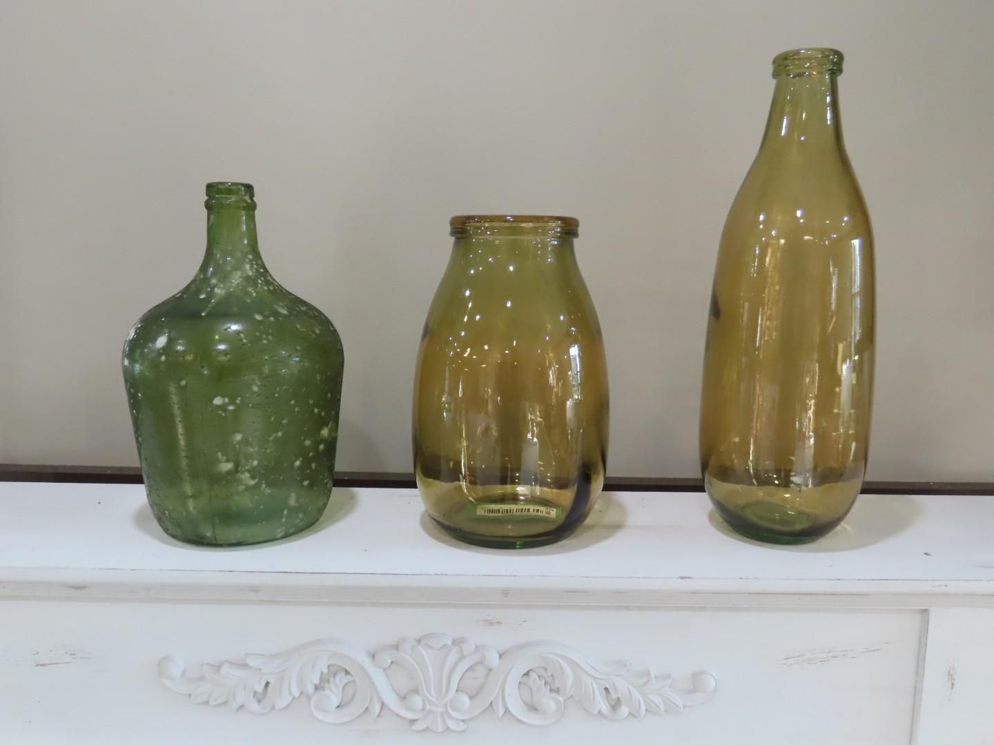 Three vintage green and amber glass bottles on a white shelf