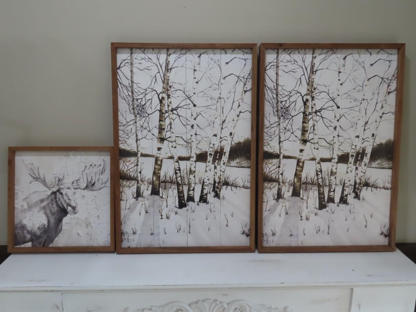 Three framed winter landscape prints on a white shelf, including a deer sketch and birch trees.