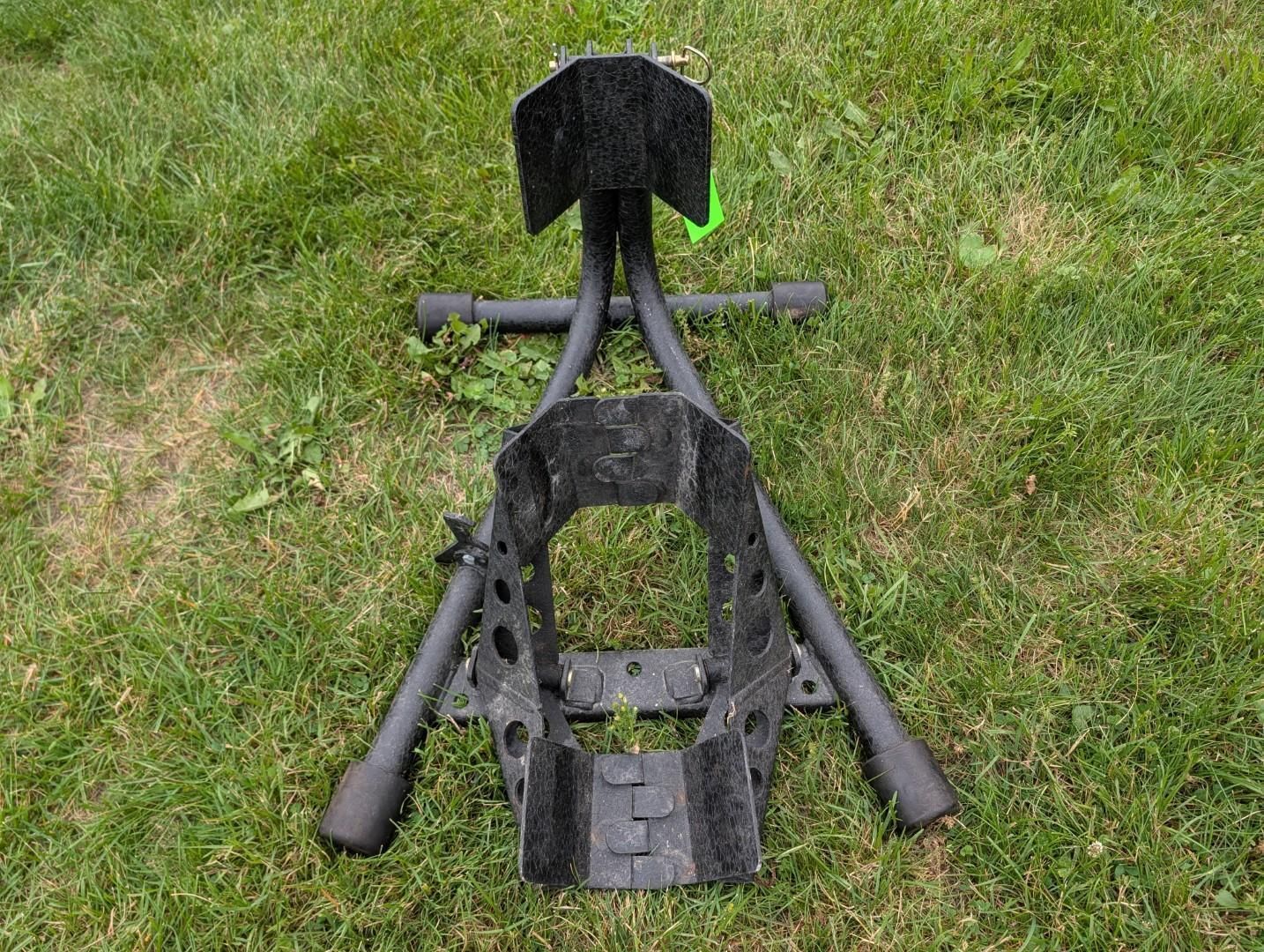 Two black metal tools or mower parts lying on grass, viewed from above