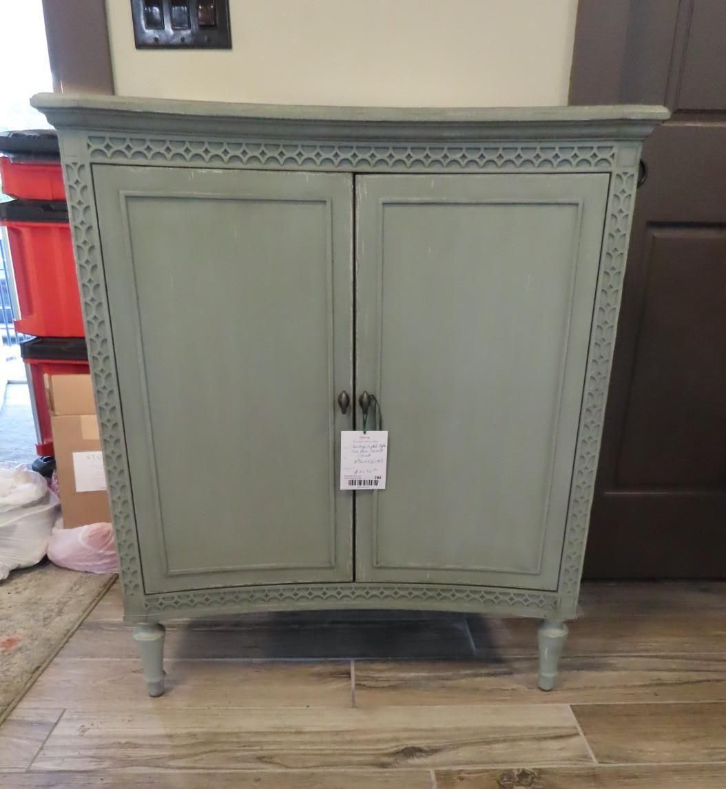 Gray-green two-door cabinet with decorative trim and a tag, standing on a tiled floor indoors