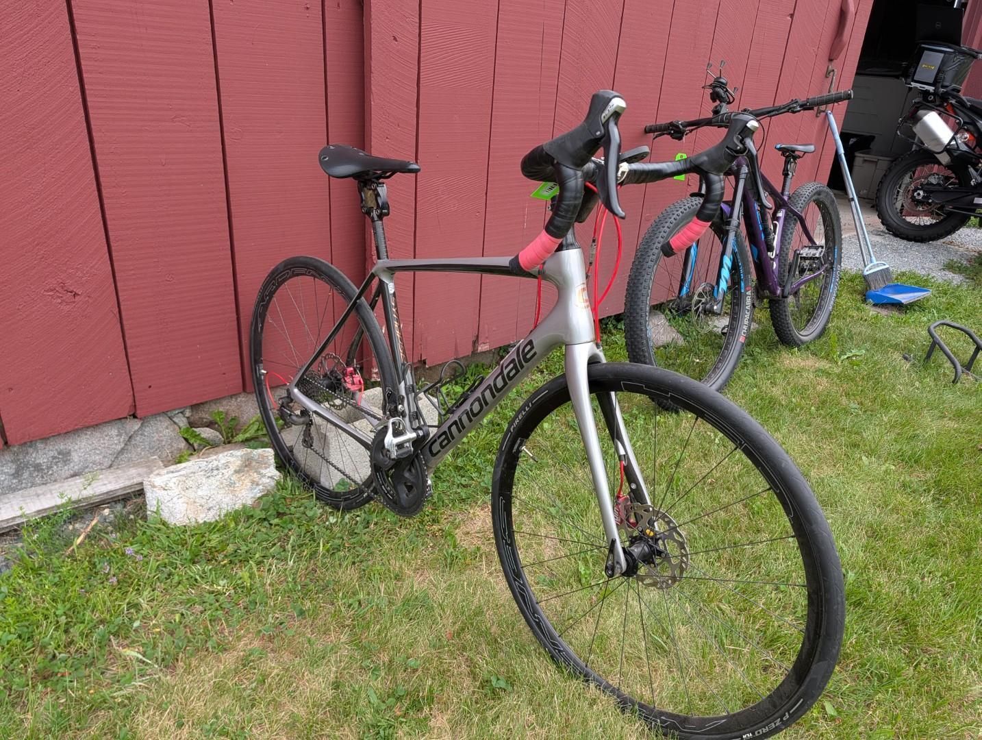 Road bike leaning against a red wooden wall, with another bike in the background.
