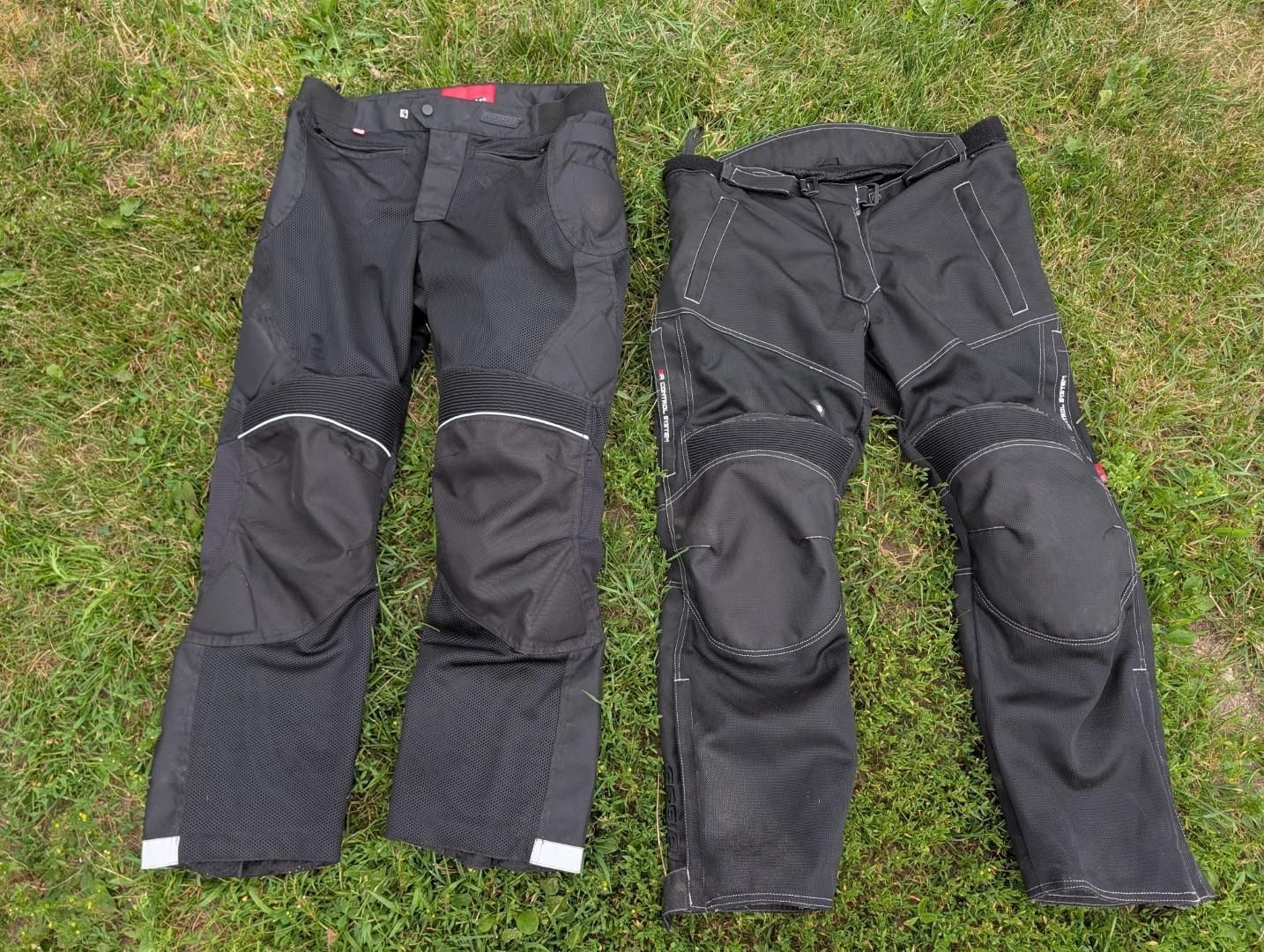 Two pairs of black pants laid side by side on grass, each with reinforced knee panels and reflective strips.