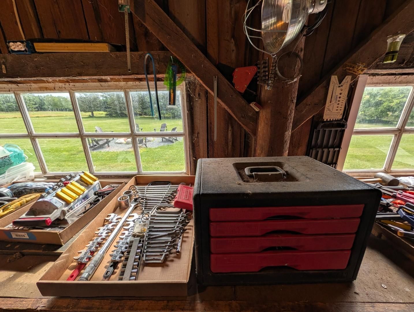 Wooden loft workbench with tools, a red drawer cabinet, and windows overlooking a green field