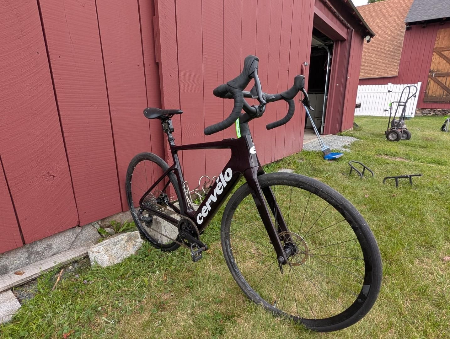 Black road bike leaning against a red barn on grass