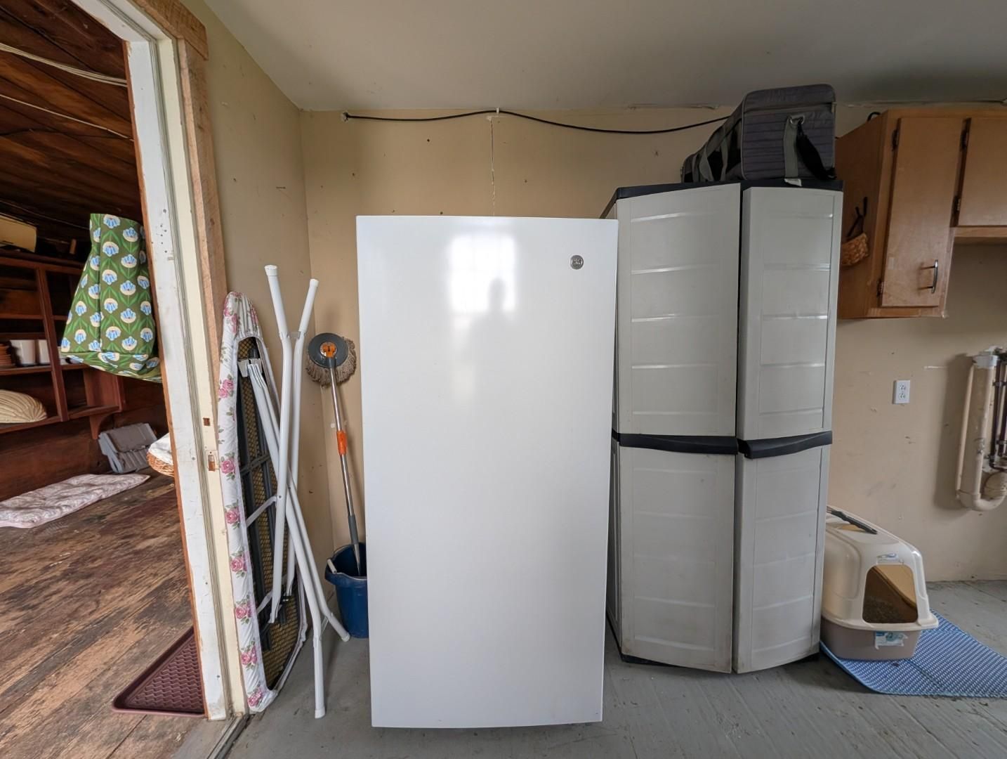 Kitchen corner with a white refrigerator, gray cabinet, and cleaning tools near a doorway.