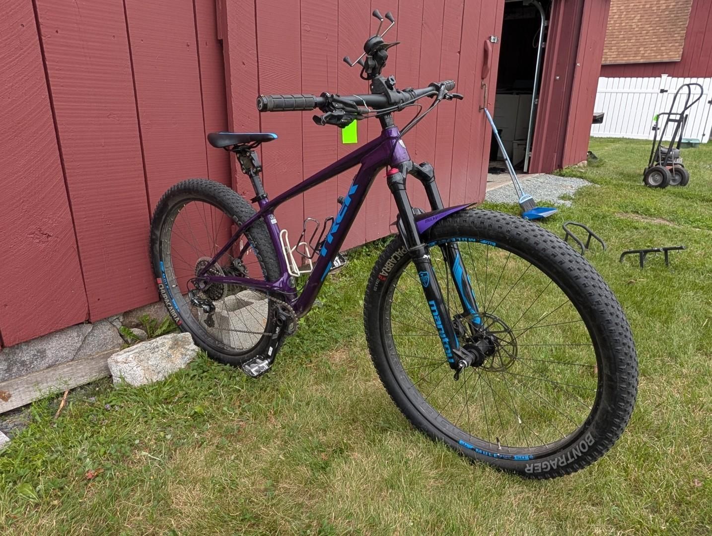 Purple-and-blue mountain bike leaning against a red shed on a grassy lawn.