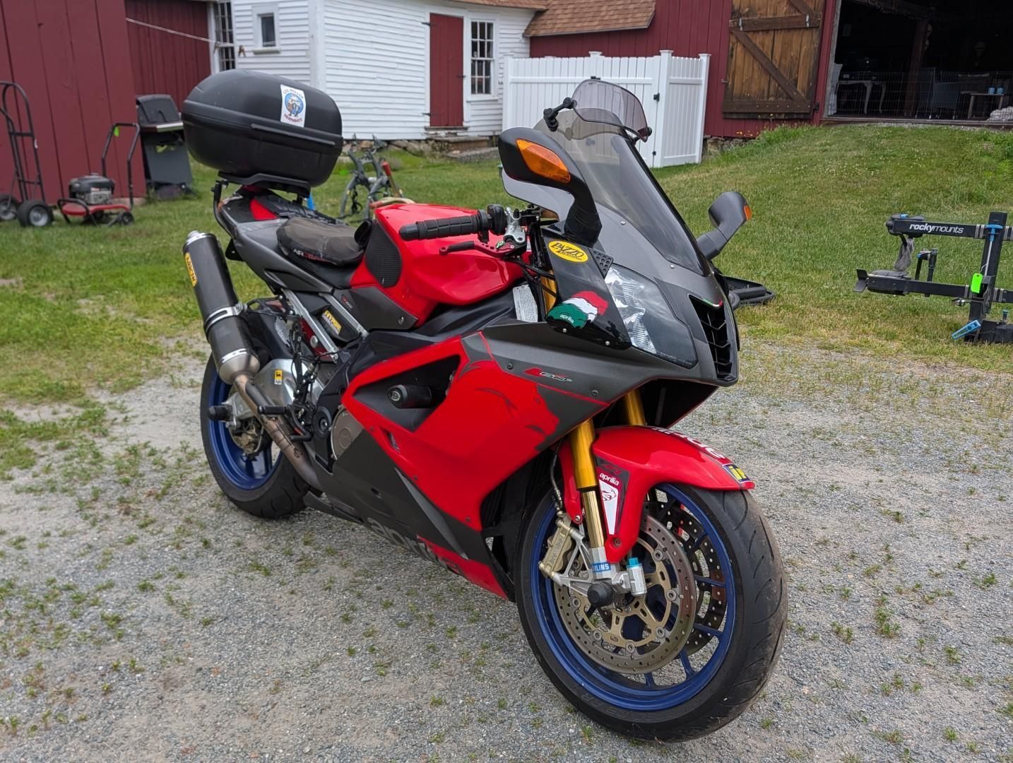 Red sport motorcycle parked on gravel in a yard, with a top case and tinted windshield.