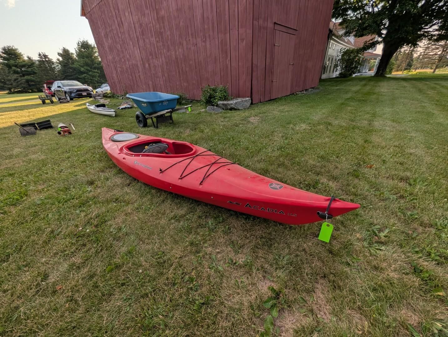 Red kayak on grass beside a barn