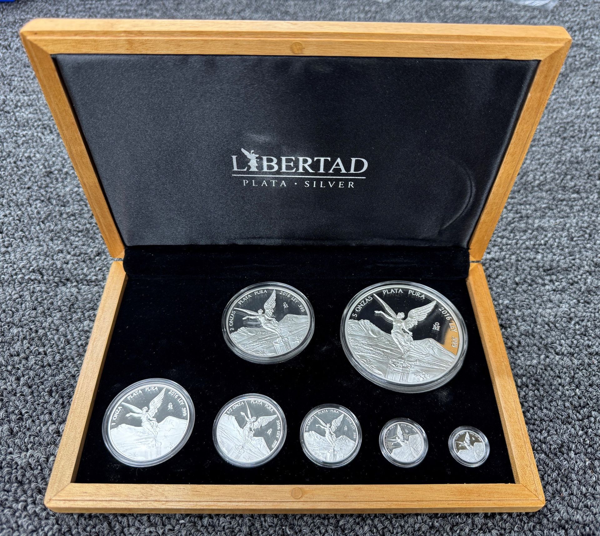 Open wooden display case with Libertad silver coins and medals on black velvet lining.