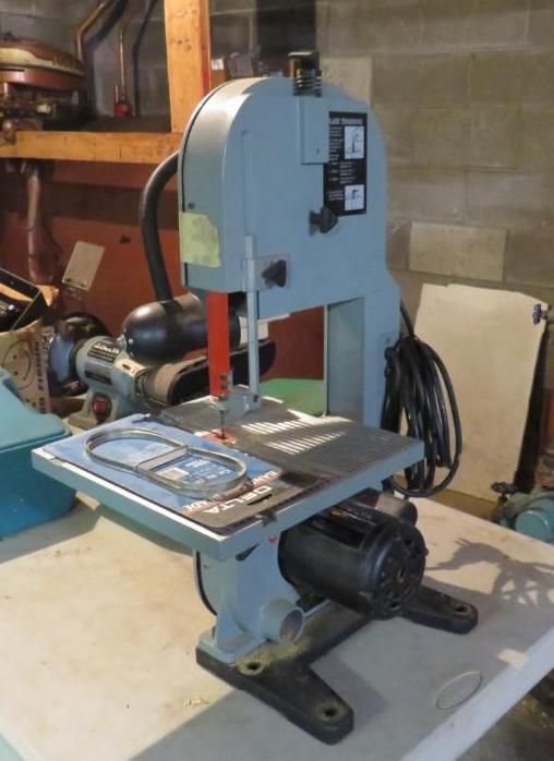 Gray bandsaw on a table, in a workshop setting.