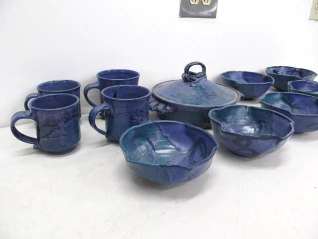 Blue ceramic pottery set on a white surface, including mugs, bowls, and a covered dish.