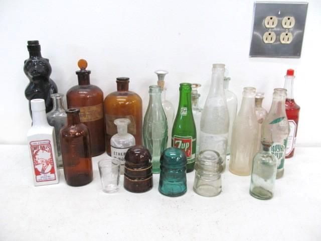 Collection of assorted vintage bottles displayed against a white wall with an electrical outlet.