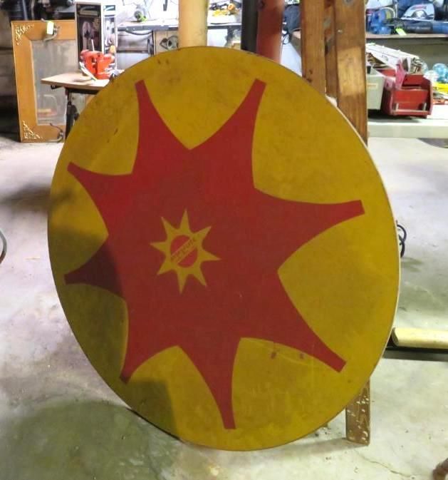 Large, round shield with yellow background and red starburst design.