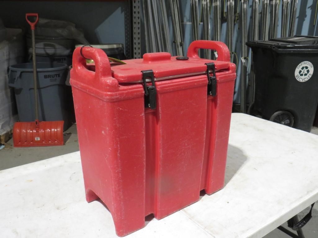 Red insulated food carrier on a white table; other objects in background.