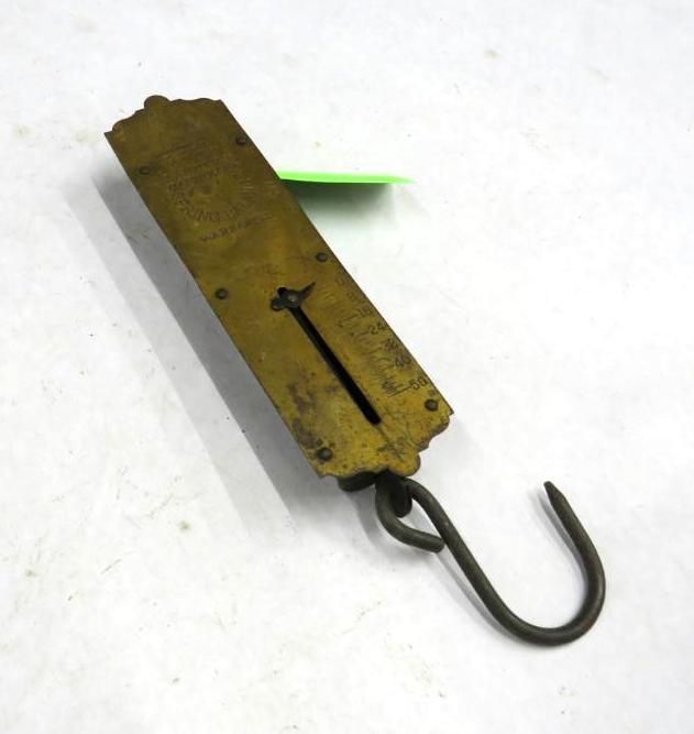 Brass hanging spring scale with hook, on a white surface.