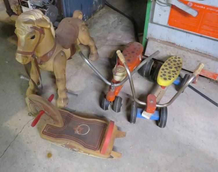 Old wooden rocking horse and two vintage tricycles on a concrete floor.