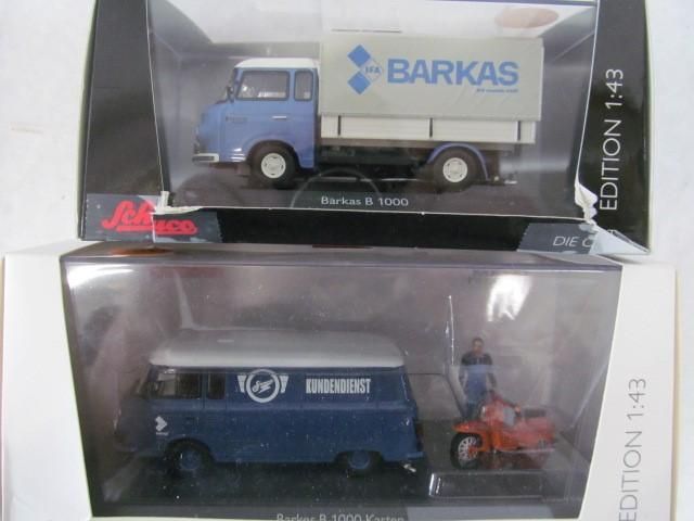 Two model trucks in boxes: a blue Barkas B1000 with a box and a blue and silver van with a scooter.