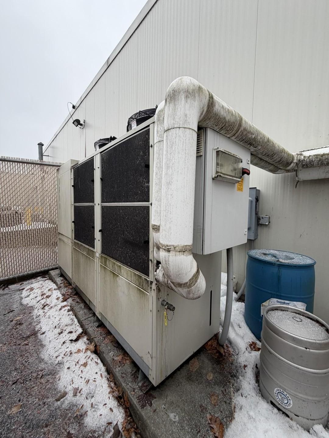 Exterior industrial HVAC unit next to a white building with snow on the ground.