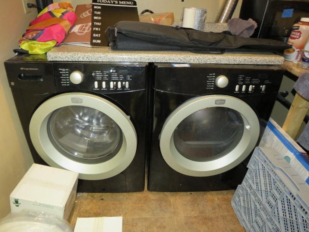 Black washer and dryer set with silver trim, on a beige floor, in a laundry room.