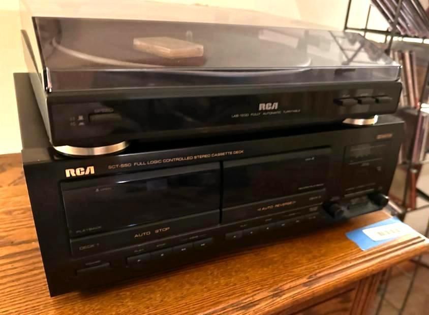 Black RCA stereo system: turntable atop a dual cassette deck, on a wooden surface.