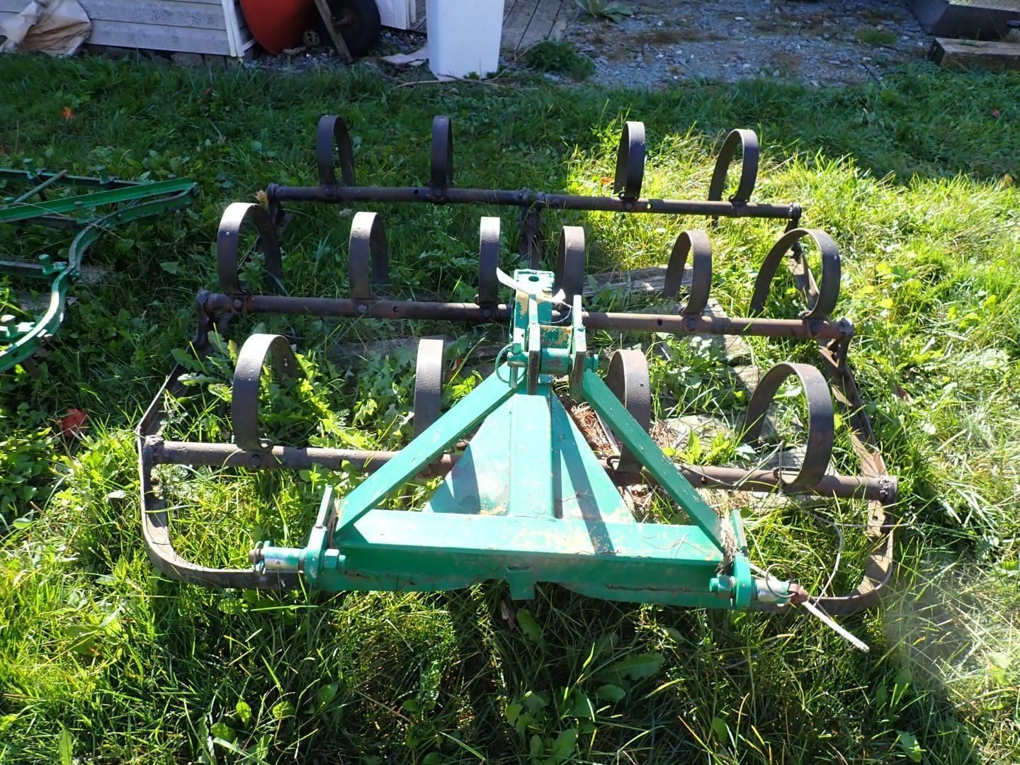 Green farm tillage implement with metal tines sitting on grass outdoors