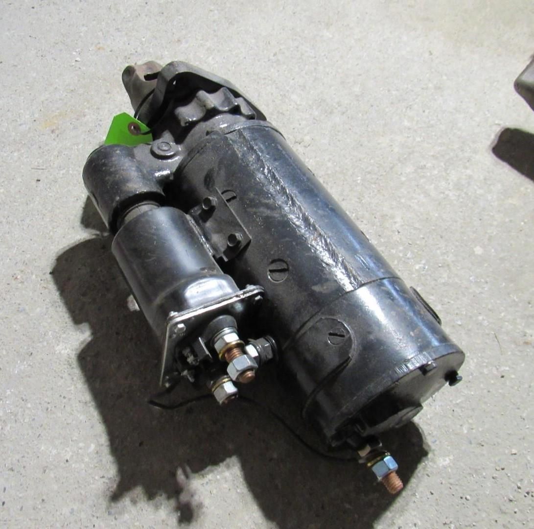 Black automotive starter motor, with solenoid attached, resting on a concrete surface.
