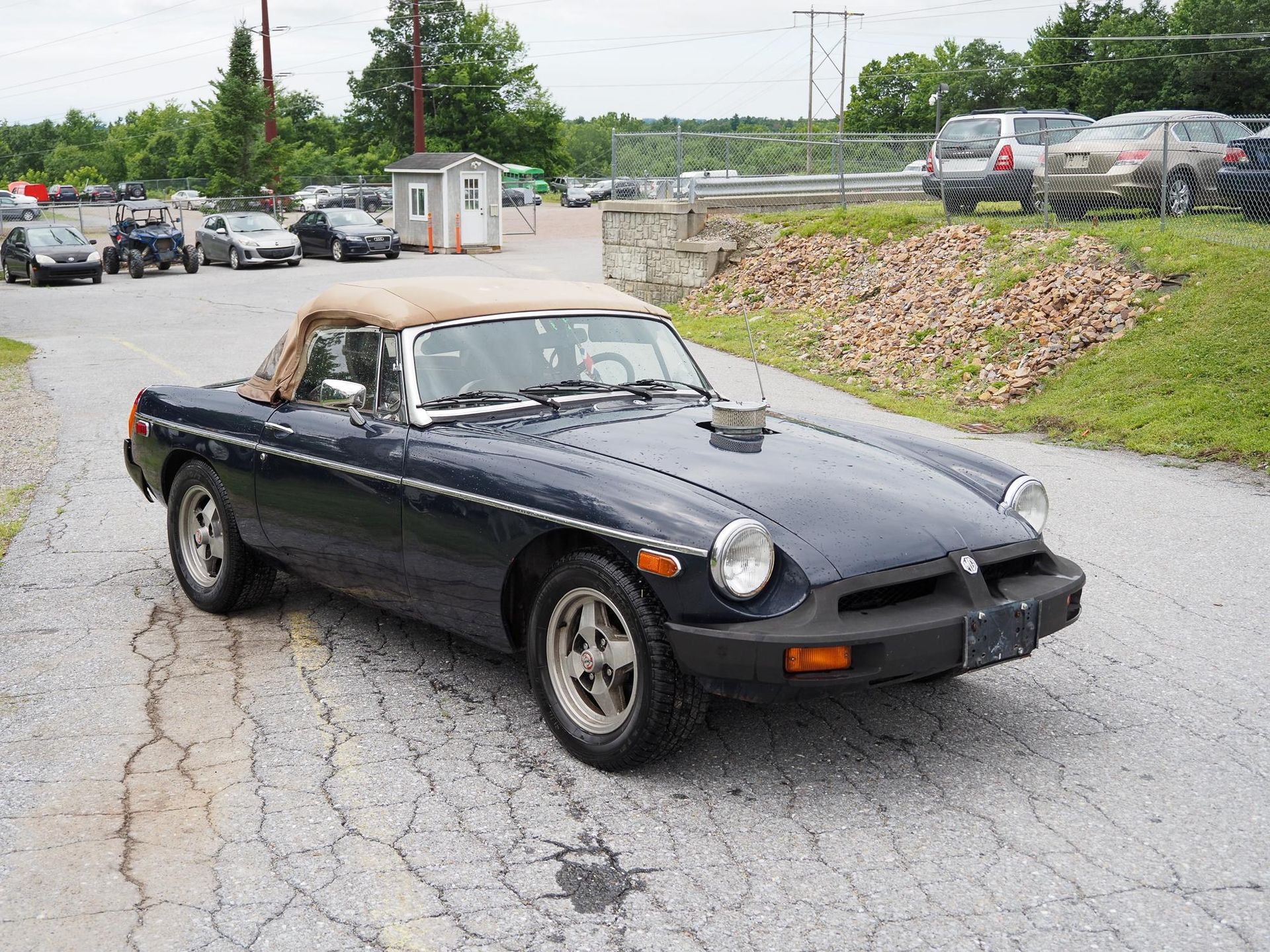 Blue convertible car parked on a gravel road, tan top, parked in an outdoor lot.
