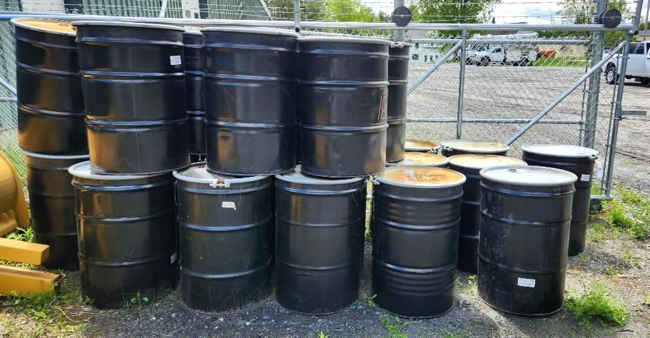 Black metal barrels stacked outdoors near a fence.