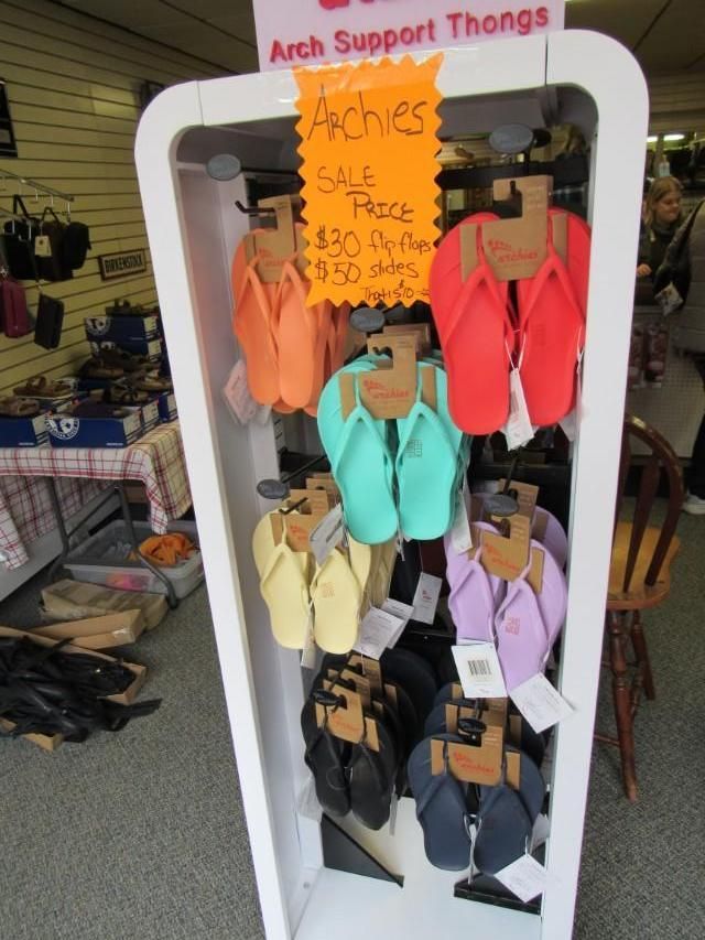Display of colorful Archies arch support thong flip-flops on a white retail stand.