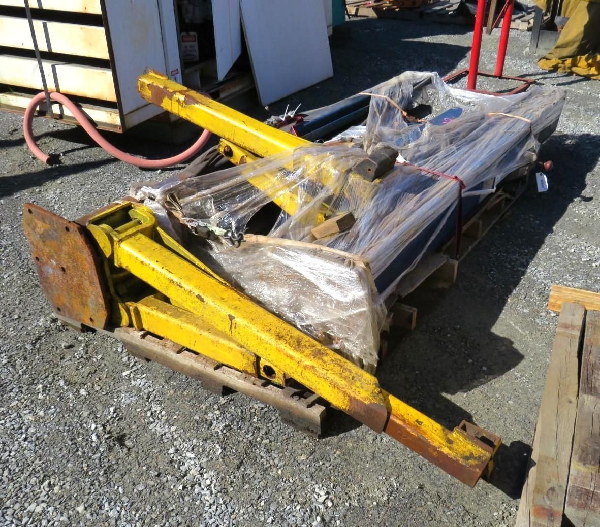 Yellow industrial equipment on a wooden pallet, wrapped in clear plastic, outdoors on gravel.