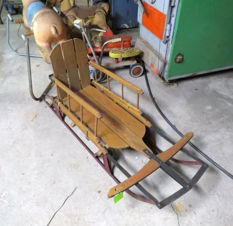 Vintage wooden child's sled with red and black metal runners, other toys in background.