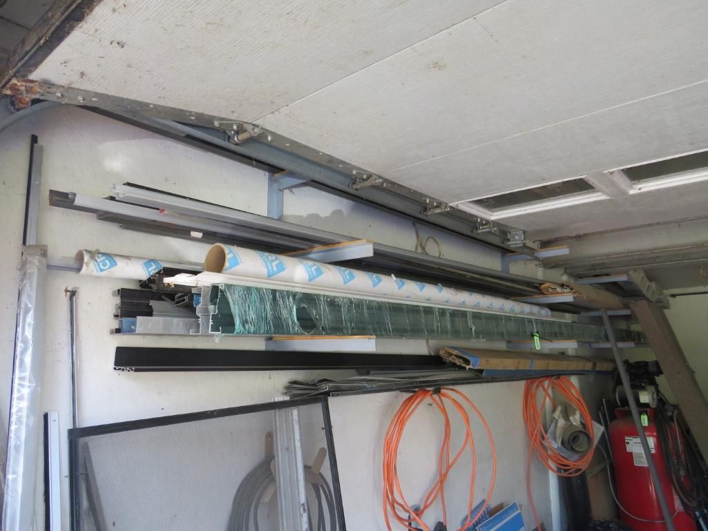 Various construction materials stored on shelves: glass panels, metal bars, and coiled cords.