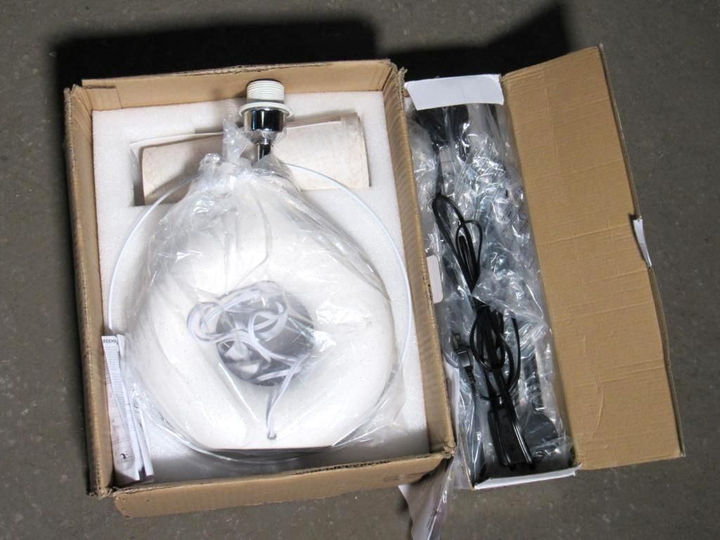 Open cardboard box containing a lamp with white shade, and a separate section with black components.