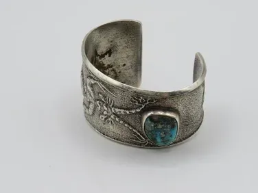 Silver cuff bracelet with turquoise stone, floral details.