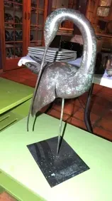 Metal bird sculpture on a green table, head bent down.