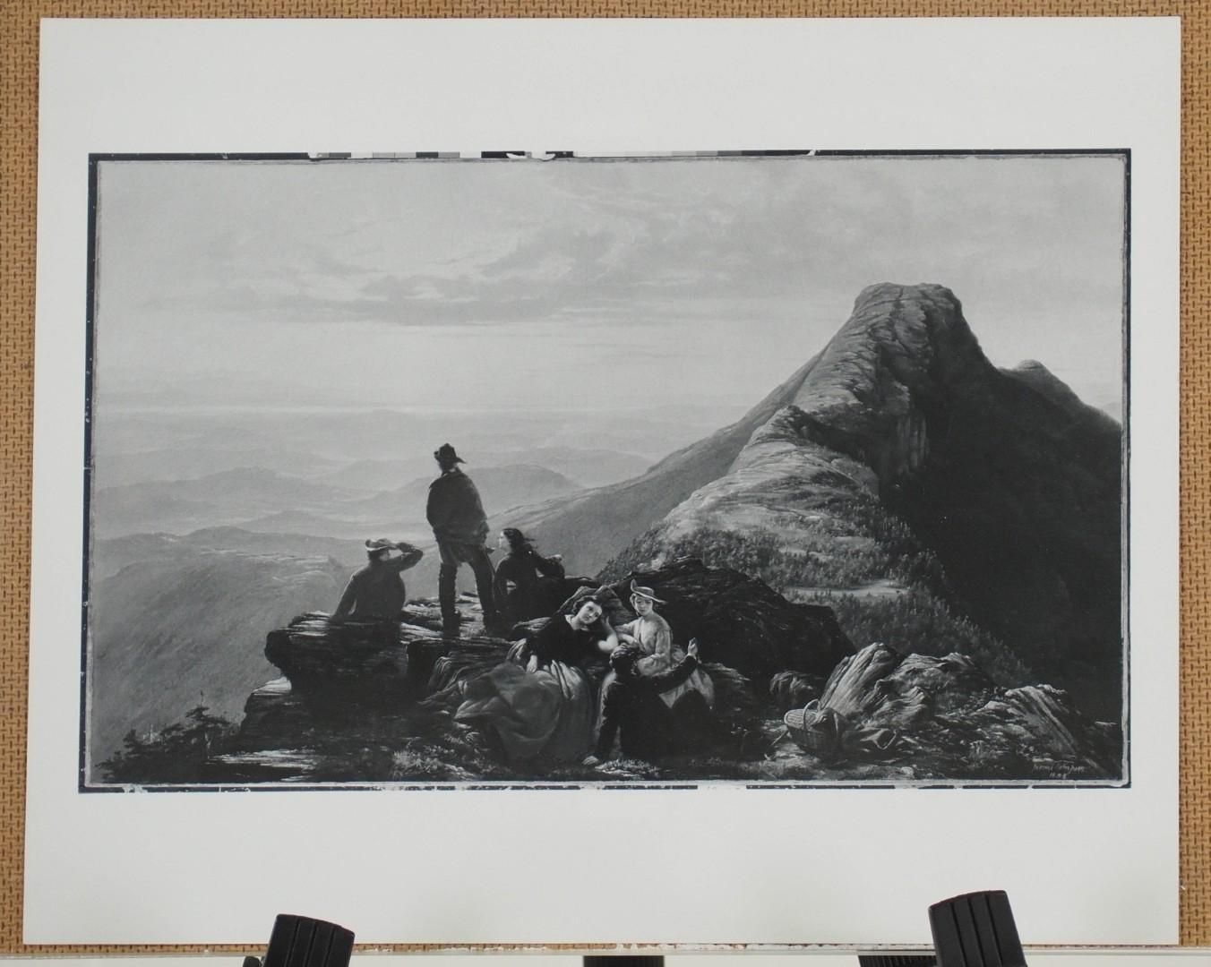 Group of people on a rocky mountaintop, overlooking a valley. Black and white photograph.
