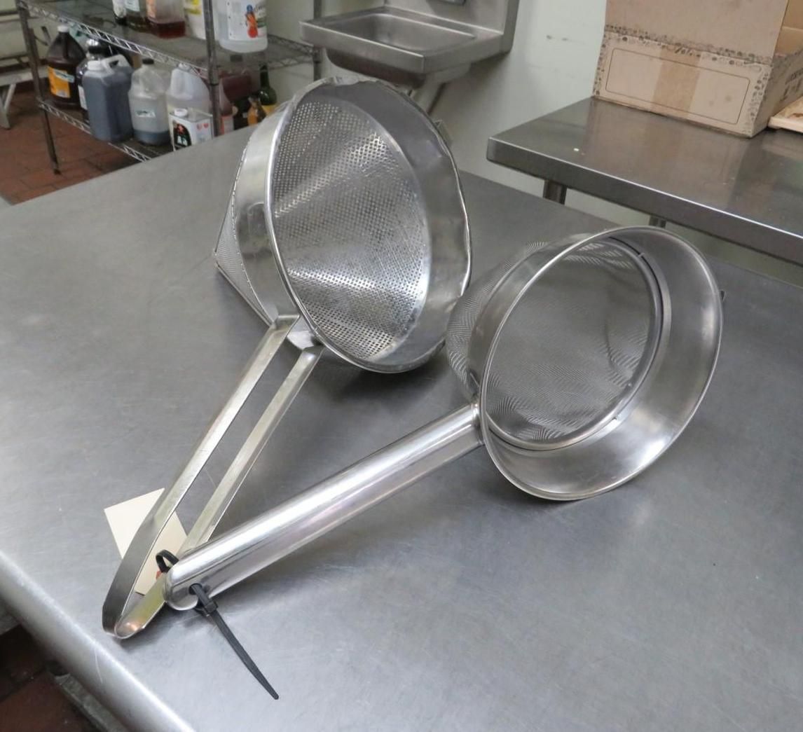 Two stainless steel mesh skimmers on a metal countertop in a kitchen.