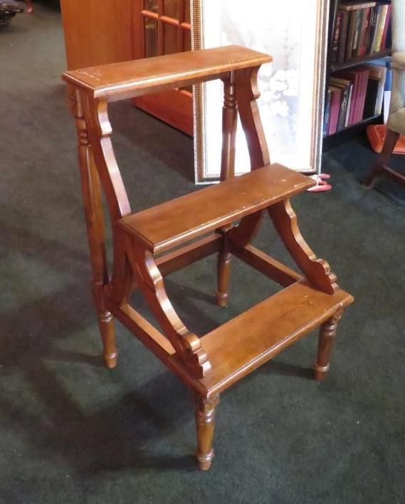 Wooden two-step step stool with ornate details, brown, indoors on green carpet.