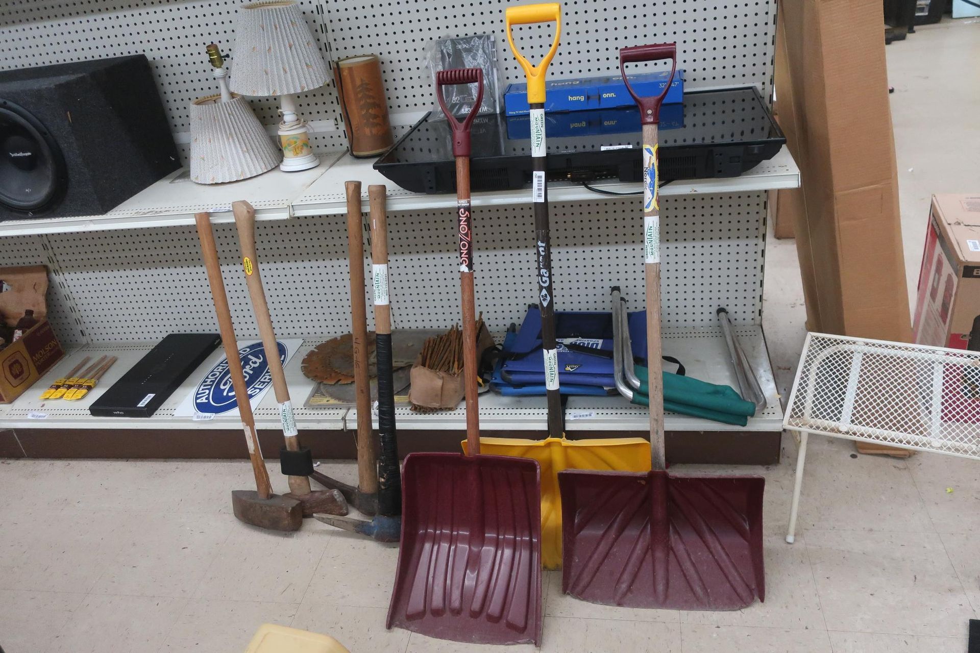 Shelves in a store with shovels, a speaker, lamps, and other items.