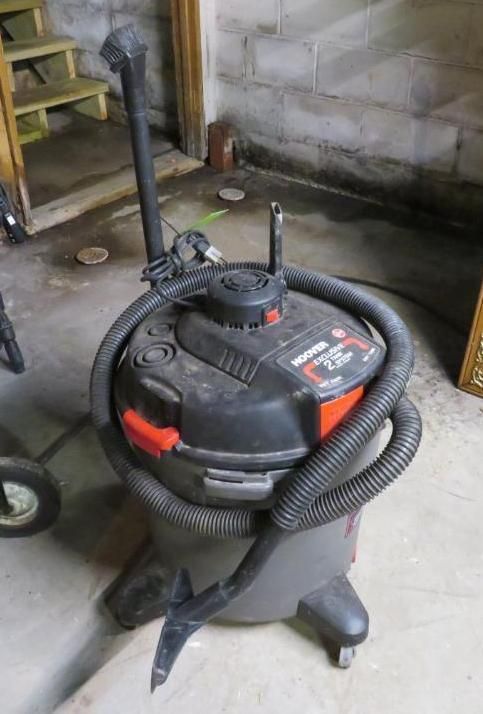 Black and gray shop vacuum with hose coiled around the body; indoors.