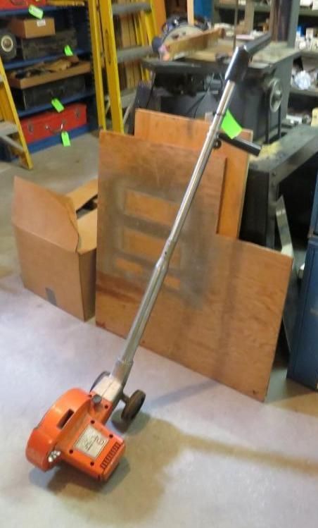 Orange floor edger with a long handle, leaning against plywood in a workshop setting.
