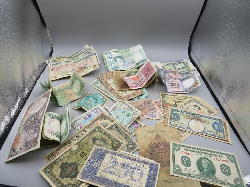Pile of international currency on a gray surface, various colors and designs visible.