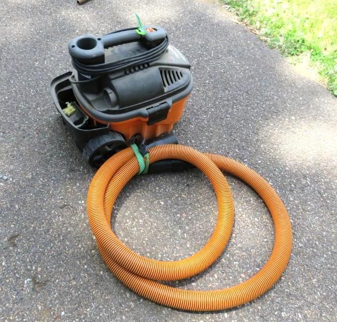 Orange and black shop vacuum with its coiled orange hose on an asphalt surface.