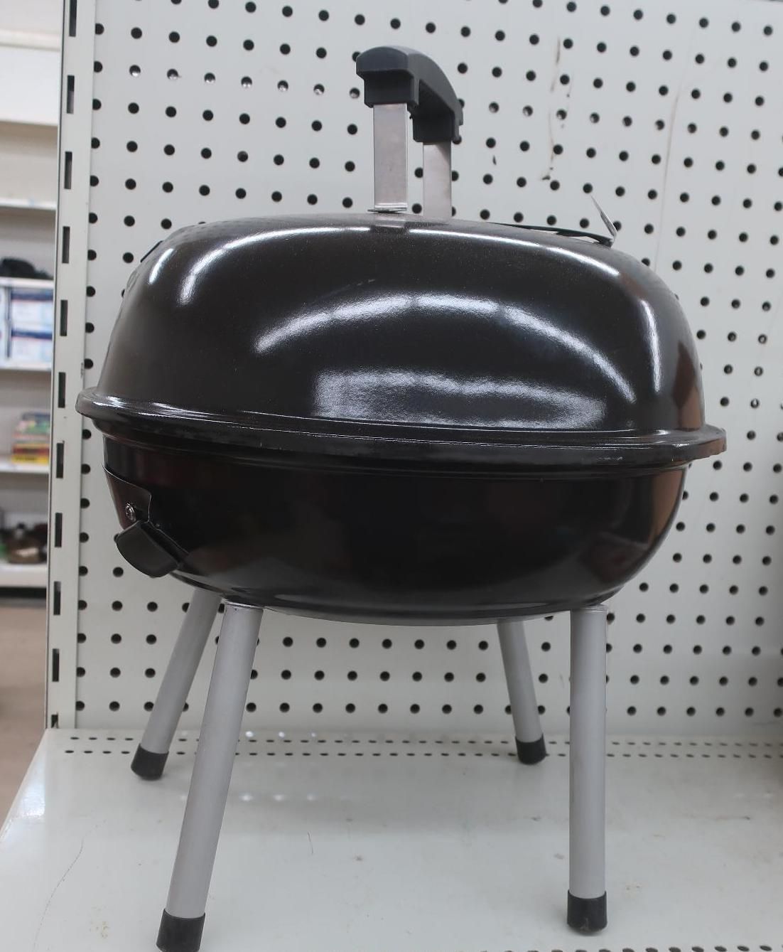 Black charcoal grill with silver legs and handle on display.